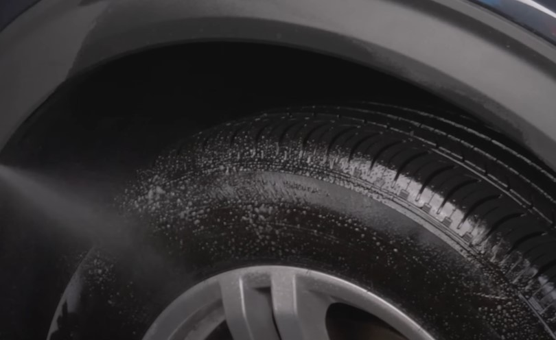 Water jets spray the tire, creating a frothy lather on its surface